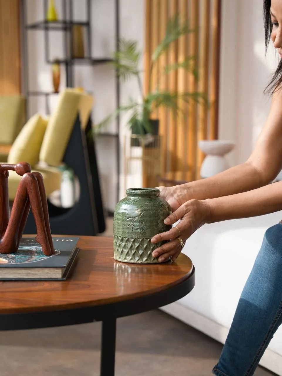 Une main pose un vase vert sur une table basse en bois